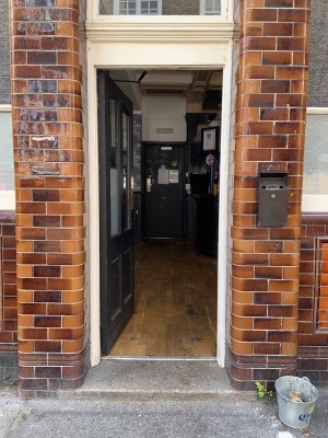 Black wood and glass door with white frame. Push from metal plate on right to open.