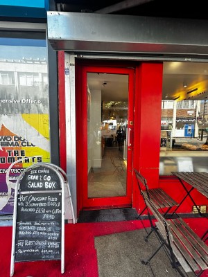 Main single glass door with red wooden frames. Silver handle on mid right. Push to open.