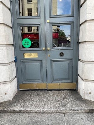 Double manual doors at main entrance with single step and doorbell for assistance on left side of doorway.
