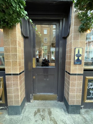 Grey wood and glass door. Push golden pad on left to open.