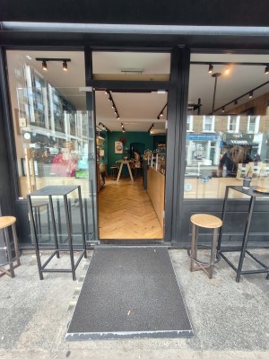 Facing black framed single glass door. Pull wooden handle on right of door to open.