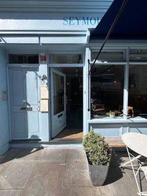 Facing door with blue frames. Push vertical silver handle on right side to open.