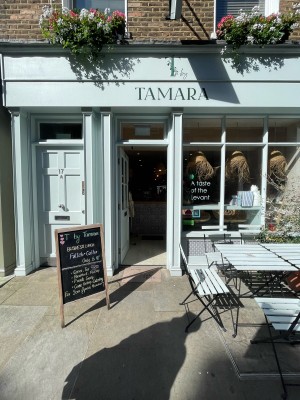 From sidewalk facing venue. Entrance straight ahead. Sandwich board to it’s left. Seating to its right.