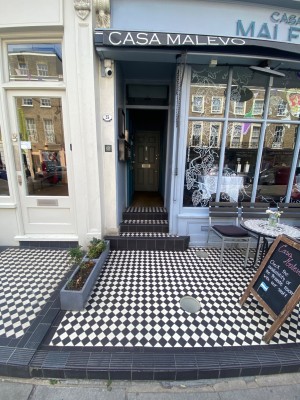 Main entrance looking straight ahead from pavement. One step before accessing outdoor area. Move forward for steps and door leading to venue.
