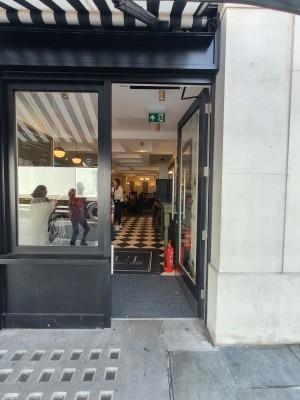 Facing single black-framed entrance door. Push silver metal vertical handle on left to open.
