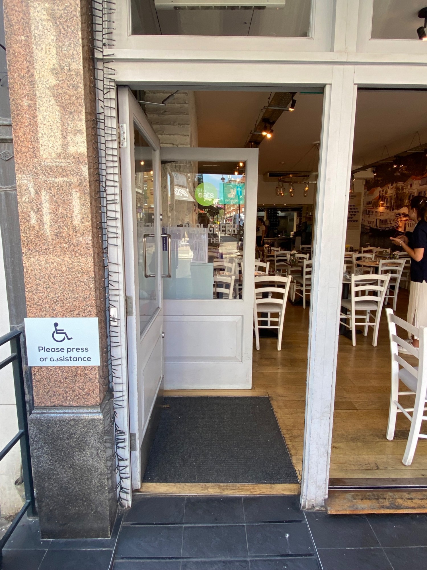 White framed glass push door with handle on right. Assistance button on left of door.