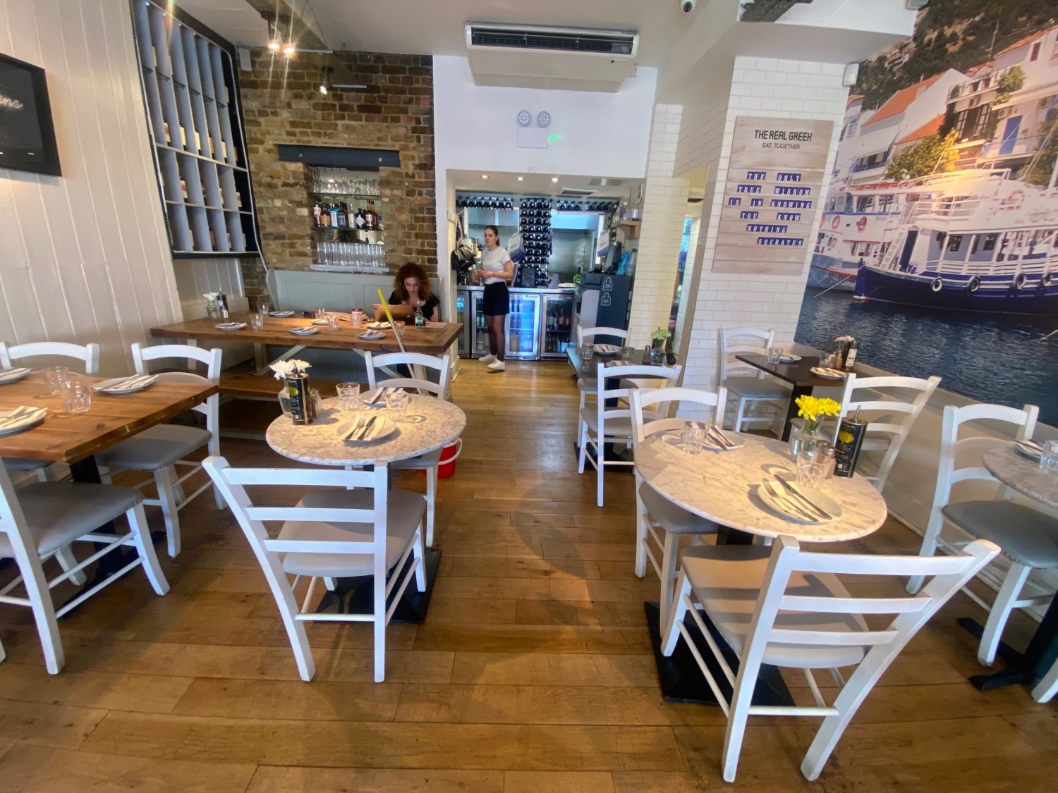 View of more chairs all sides. By back left wall, bench. Open kitchen back wall straight ahead.