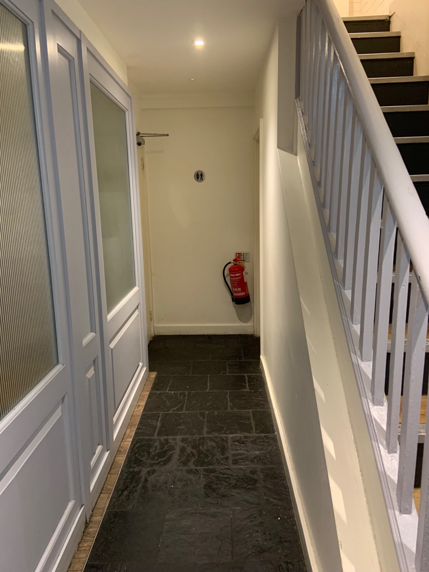 View from bottom of stairs looking to back along left side of stairs. Pathway to bathrooms straight ahead.