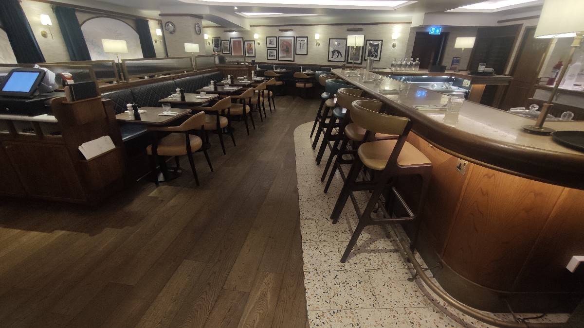 From bottom of staircase facing straight. Bar area with stools along right. Main path in centre. Half booths along left.
