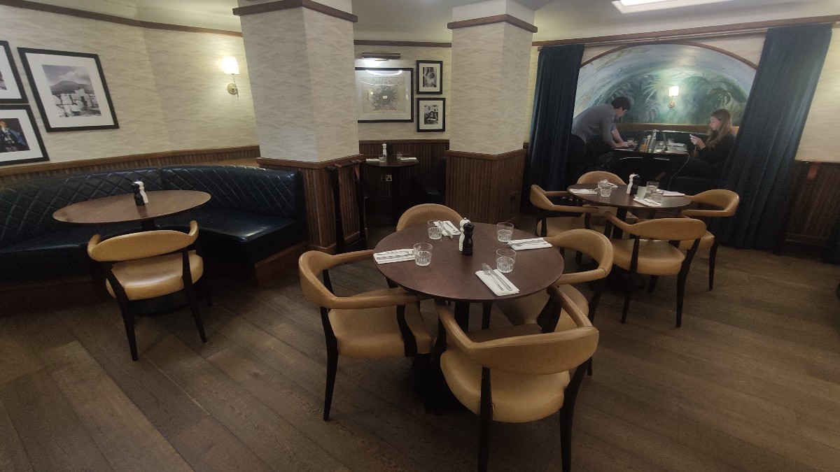 From bottom of staircase facing back left. Half booths at left. Path ahead. Tables and chairs in centre.