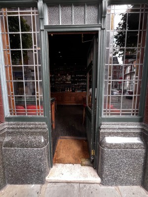 Facing entrance. Push metal hold area on left of door with green frames and a glass window to open.