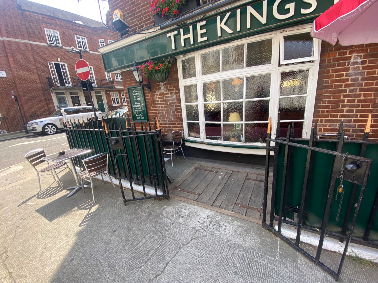 From left of main entrance, facing straight. Black iron gates ahead. Pull gates at centre to open. Table and chairs to left of gates.