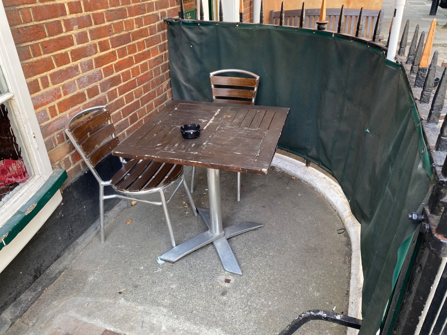 From inside gate, facing right. Fence along right. Table and chairs ahead. Wall on left.