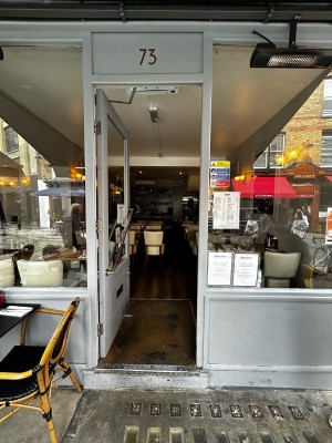Glass door with white wooden frames. Silver handle across centre. Push on right to open. Seating to left of entrance.
