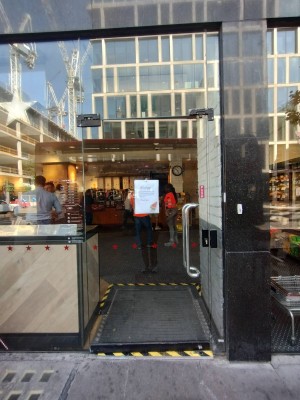 Facing single glass entrance door. Push silver metal handle on right of door to open.