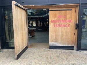 Brown wooden doors with pink writing. Intercom and badge scanner on right. Left door swings open from right.