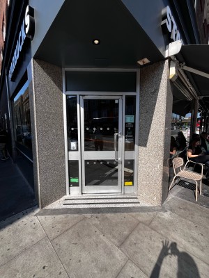 Glass door with silver frames. Push silver vertical metal handle on right to open.