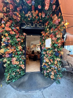Single black wooden door with glass panels. Flowers and plants form arch around doorway. Push from left to open.