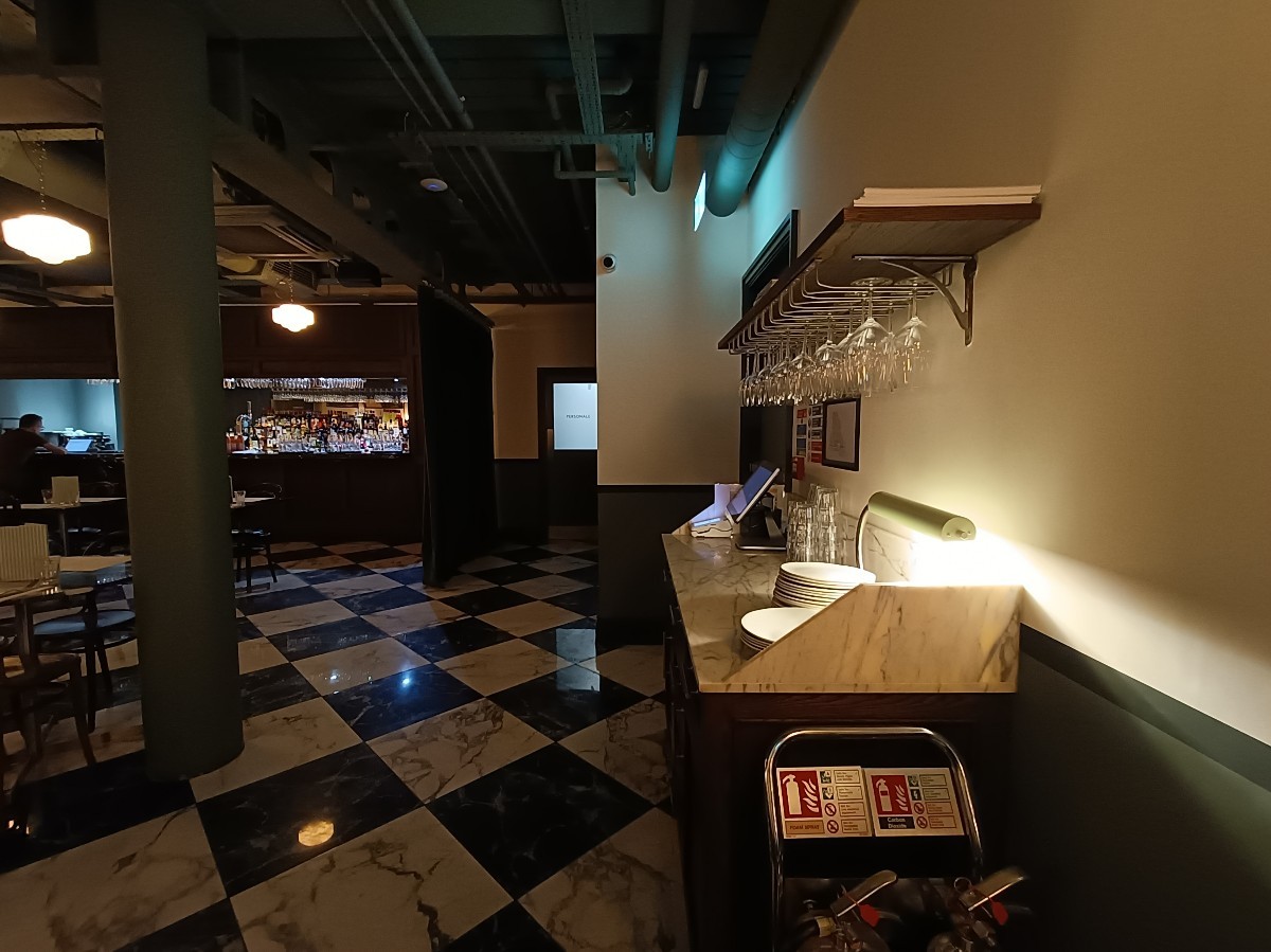 From end of pillar, looking straight. Host desk on right. Path in middle. Pillar on left. Bar at back left.