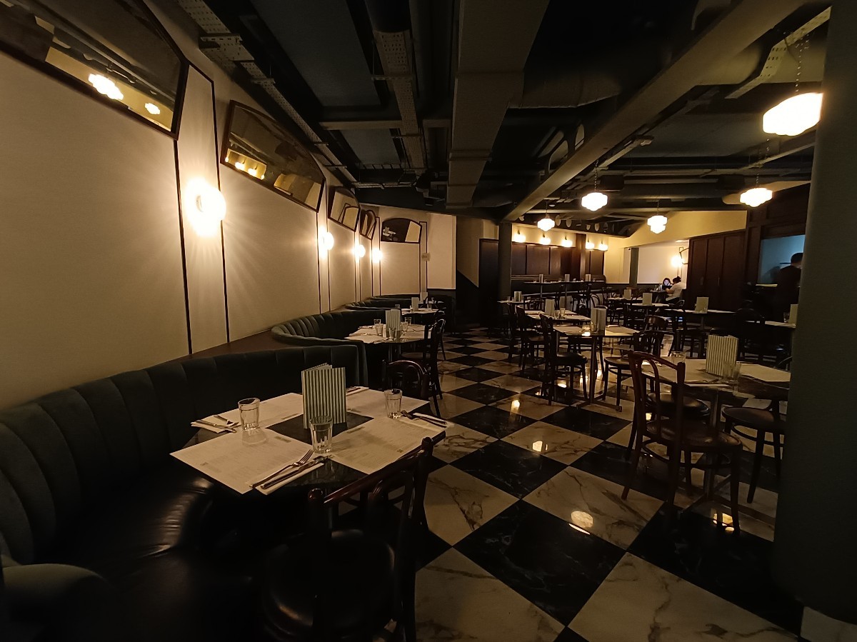 From end of pillar, looking left. Half-booths and chairs along left. Tables and chairs behind pillar on right. Path in middle.