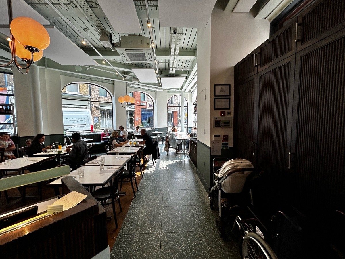 From entrance, facing right. Host desk on left, followed by chairs and tables. Path ahead leading to more seating.