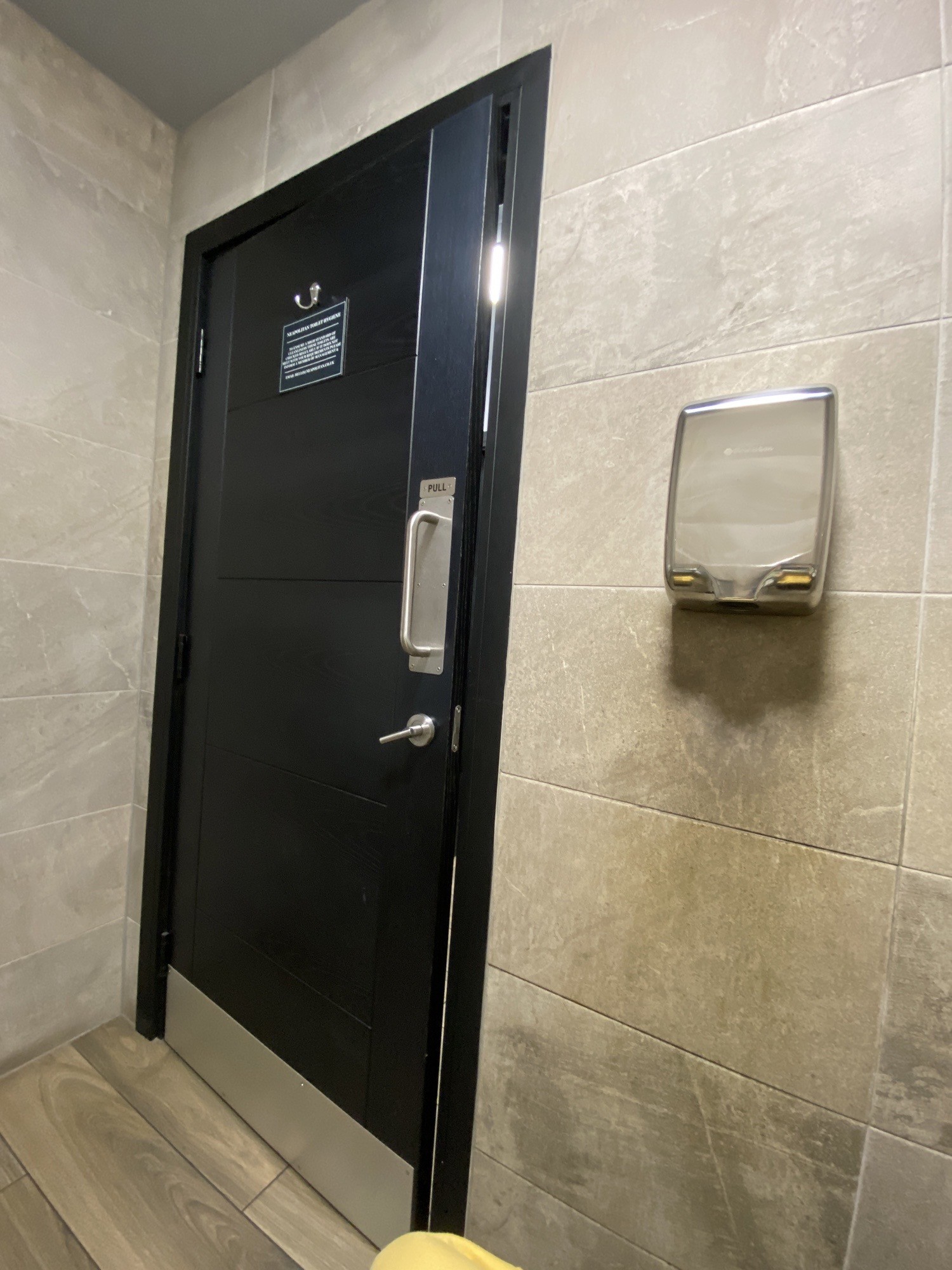 Back of the bathroom door vertical bar handle on right hand side of the door, lock below handle pull open. Hand drier to right if the door. High coat hooks on the door