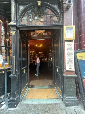 Preceding wooden black doors, then second set of brown wooden doors with large glass panels. Push black and gold metal handles in middle to open.