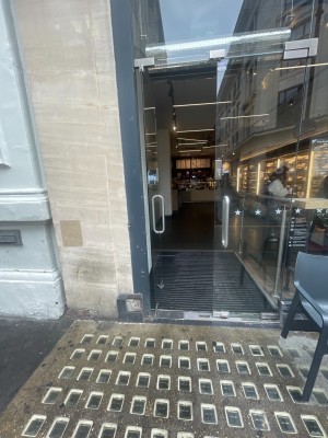 From street looking straight at door. Double glass door with handles in the middle. Small bumps and in built ramp.