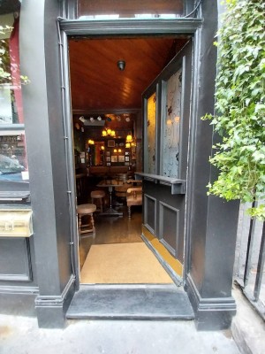 Single dark grey wooden door with large glass panels. Grey table runs across centre of door. Push from left to open.