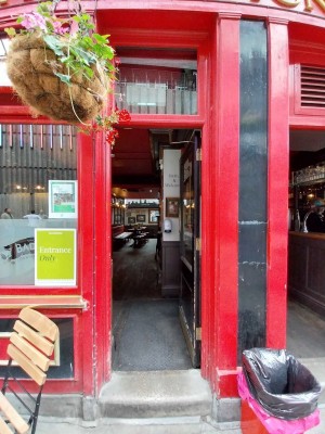 Single black wooden door with large glass panel. Gold pad on left, push to open.