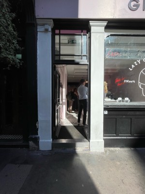Facing entrance. One metal step before door. Black wood-panelled glass door ahead. Push silver doorknob on right to open.