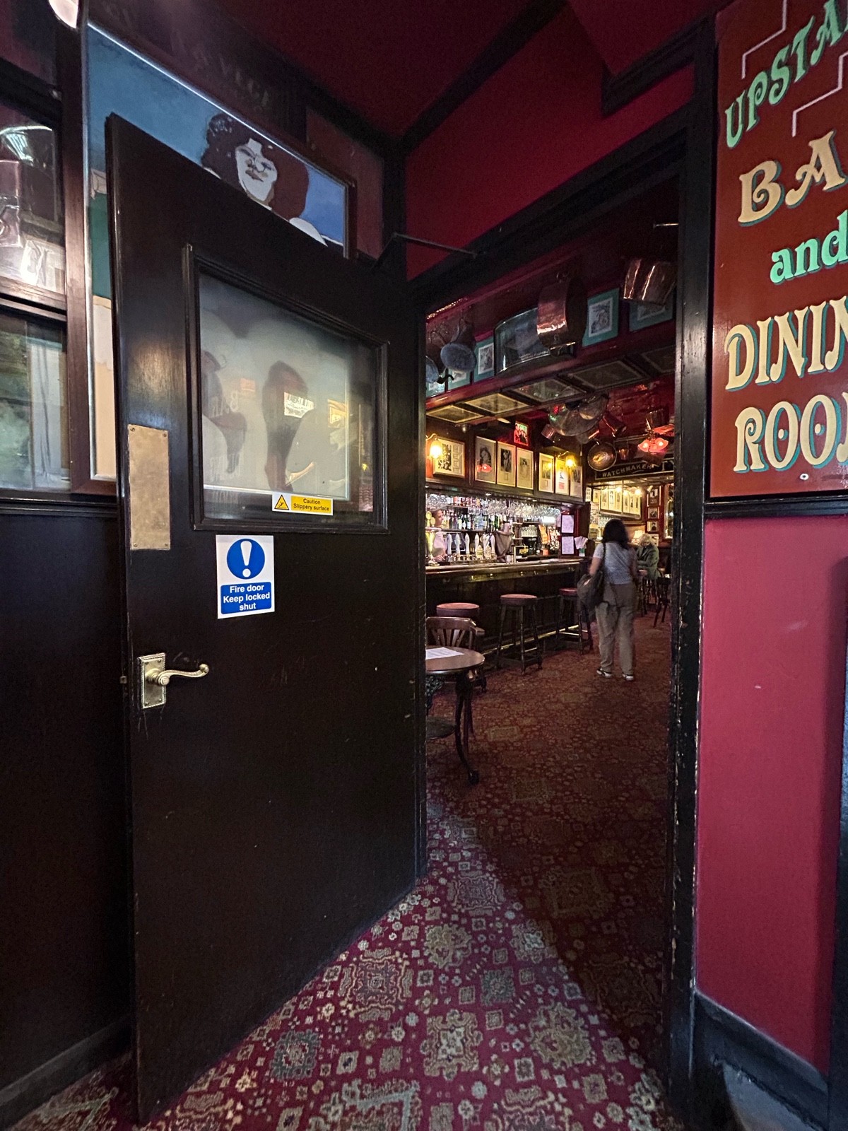 From first doorway facing left. Single black wooden door on right with glass panel and small gold metal handle. Pull from right to open.