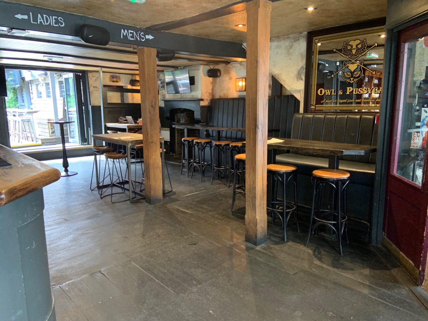 View from end of bar counter looking to back right corner. Seating along uneven right wall. Limited seating and two pillars in front of space. Wide pathways leading to outdoor area to back right.