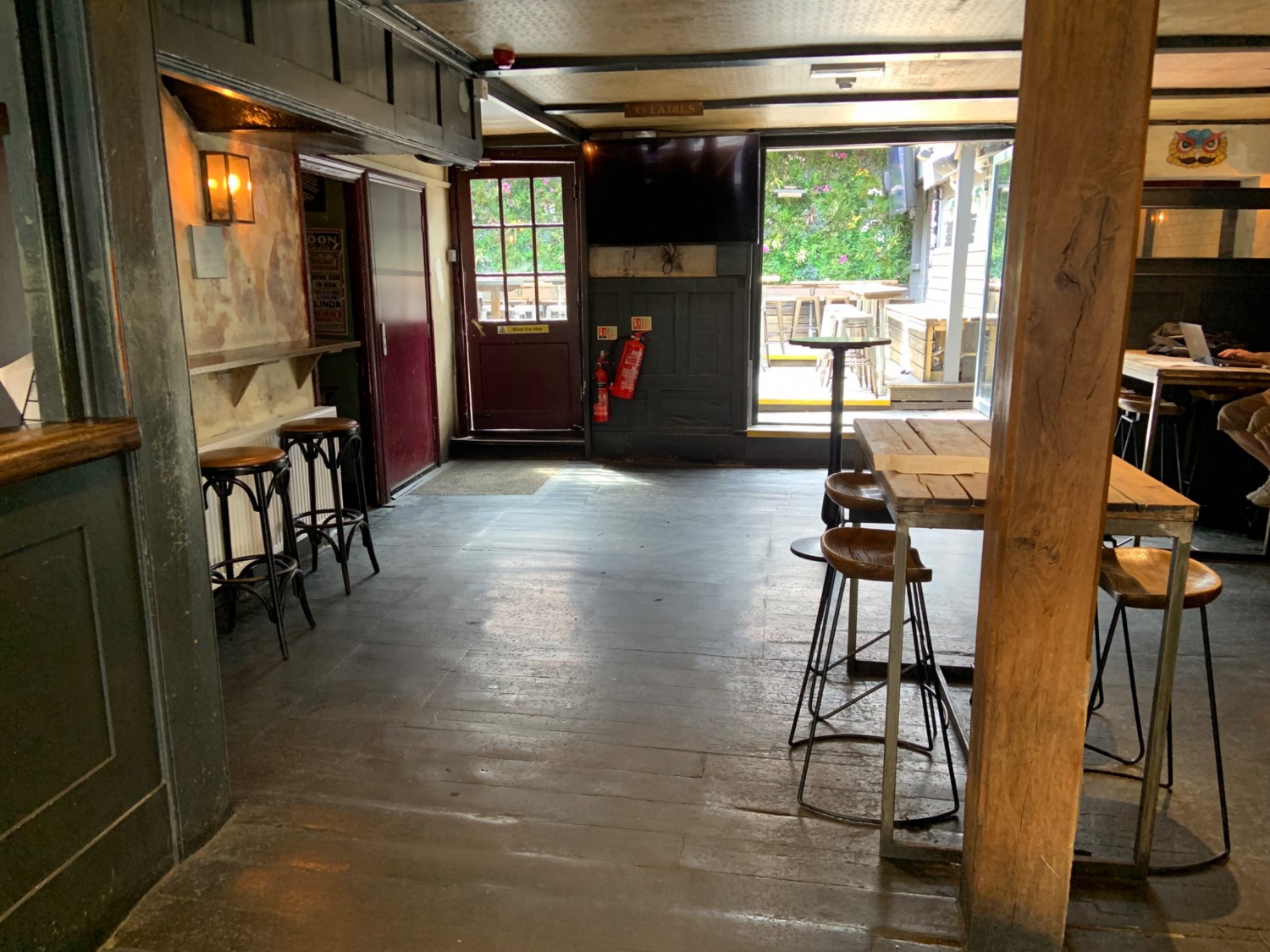 View from end of bar looking to back wall. Door to toilet in back left with seating in front along wall. Wide pathway centre. Seating to right. Door to outdoor area in back right.