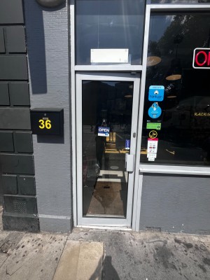 Single glass door with grey metal frame. Push grey metal handle on right to open.