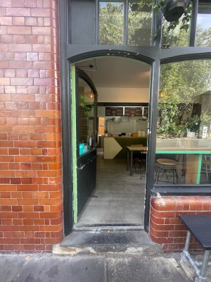 Glass door with black wooden frame ahead. Push golden metal handle on right to open.