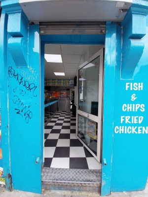 Glass door with blue frame and metal handle on left. Push to open.
