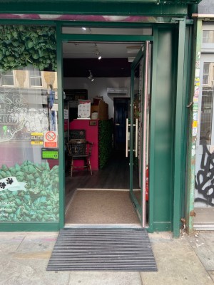 Glass entrance door with dark green frame. Push vertical gold handle on left to open.