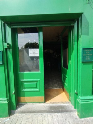 Double green wooden door with glass panels. Push right one open from middle to right. Small and very small step on top at entrance. Small bump after door.