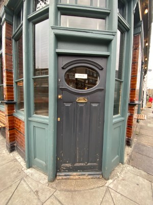 Black wooden door with glass panel ahead. Push gold metal handle on left to open.