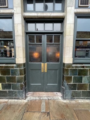 Grey wood-panelled glass door. Push brass plates at centre to open.