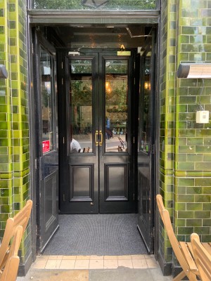 Black frame glass doors. First set of doors push to open from centre where doors meet. Second directly after pull to open from centre where doors meet.