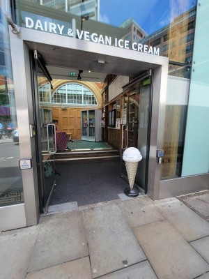 Double glass doors. Handles center. Pull to open or automatic buttons to left and right of door. Pathway after doors.