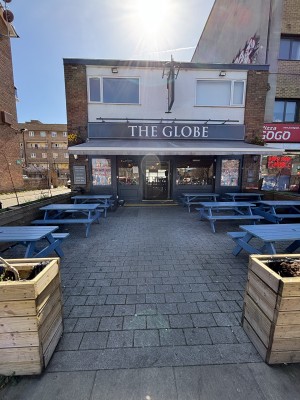 From sidewalk facing venue. Opening ahead between planters. Path down center to entrance on back. Outdoor seating along both sides.