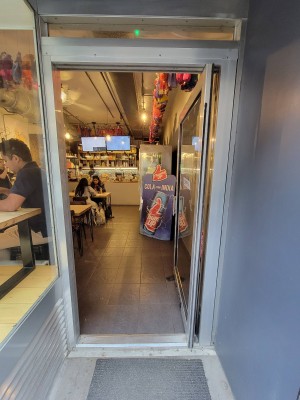 Facing single glass door. Push metal handle on left to open.