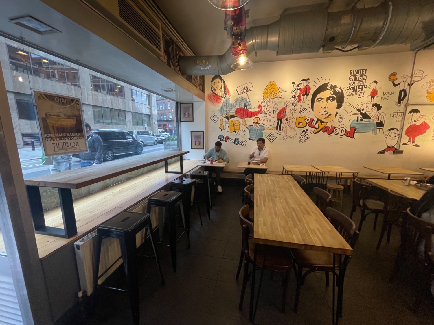 From entrance facing left. High tables and stools along left. Tables and chairs on right in center space. Benches and tables along back.