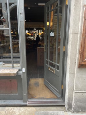 Glass door with grey frame ahead. Push door to open via golden handle on left.
