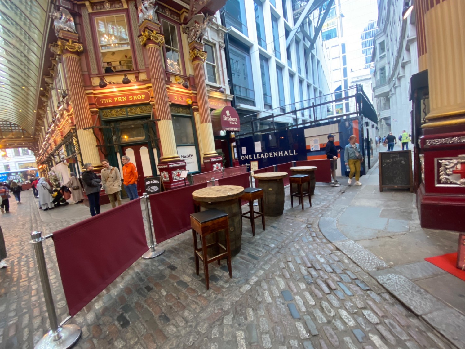 Outdoor area on left side of entrance. High barrels with stools in front of material barricades. Pathway on right.