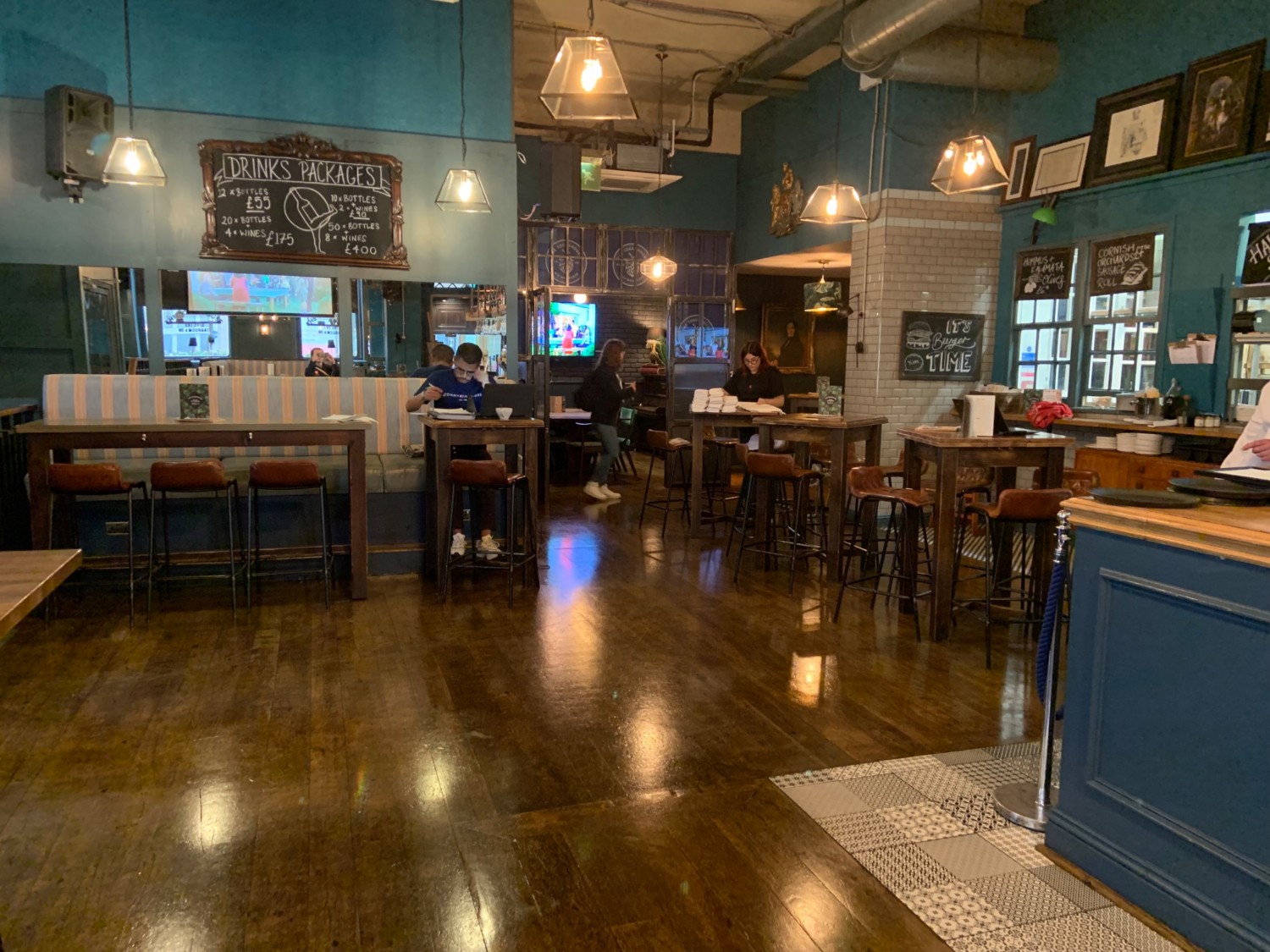From end of bar looking straight, seating along back left and clustered to back right. Wide pathway in front leading to side seating area.
