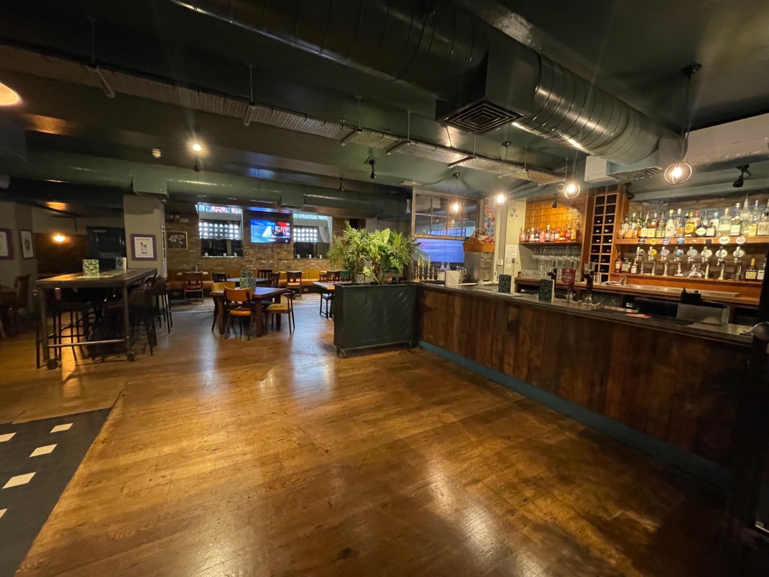 From the beginning of the downstairs area looking slightly left. Bar area on right. Wide central pathway. Behind tables and chairs.